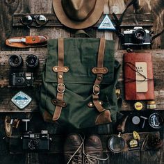 a green backpack sitting on top of a wooden table filled with assorted items next to a hat