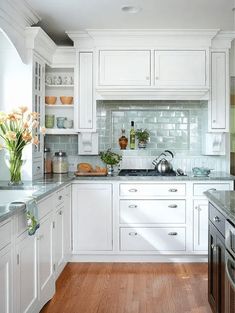 a kitchen with white cabinets and wood floors is pictured in this image, there are flowers on the counter