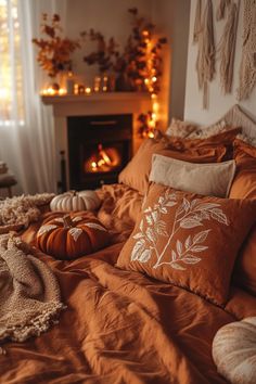 a bed covered in lots of pillows and blankets next to a fire place with pumpkins on it