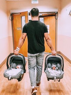 a man walking with two baby strollers in his hands while holding onto the handles of their carseats