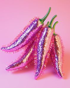 three purple and pink hot peppers on a pink background with glitter sprinkles