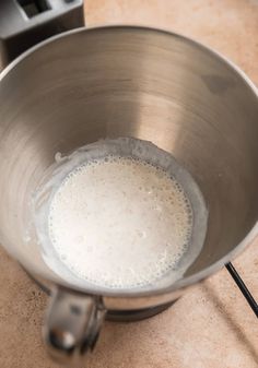 a metal bowl filled with white liquid on top of a counter next to a blender