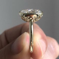 a close up of a person's hand holding an engagement ring with a diamond in it