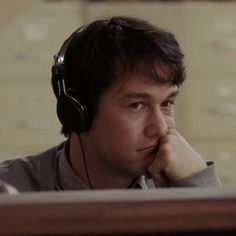 a man wearing headphones sitting in front of a computer monitor with his chin resting on his hand