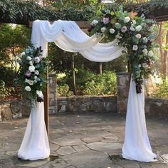 an outdoor wedding ceremony with white draping and flowers on the arch, surrounded by greenery