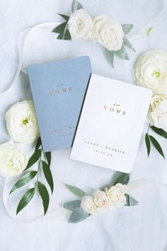 two notebooks sitting next to each other on top of a white flower covered table