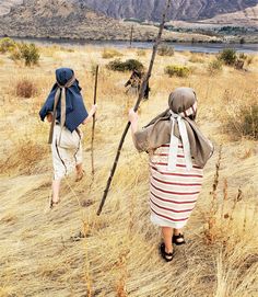 two people are walking through the dry grass with backpacks on their back and one is carrying a pole