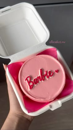 someone is holding up a pink cake in a foam container with the word barbie on it