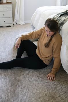 a woman sitting on the floor in front of a bed wearing black leggings