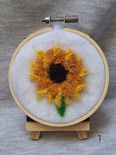 a sunflower is shown in the middle of a embroidery project on a wooden stand