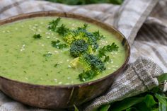 a wooden bowl filled with broccoli soup on top of a cloth covered table