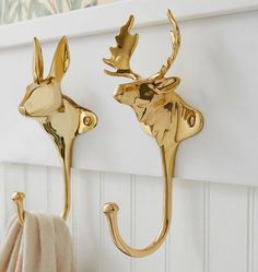 two gold deer hooks on a white wall next to a towel rack with towels hanging from it