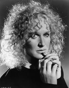 a black and white photo of a woman with curly hair holding her finger to her lips