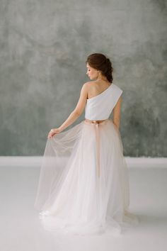 the back of a woman wearing a white one shoulder dress with a pink sash around her waist