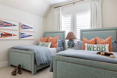 two beds in a bedroom with orange and blue pillows on them, next to a window