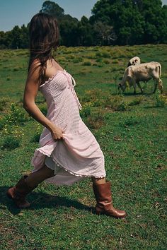 a woman in a pink dress is running through the grass with two cows behind her