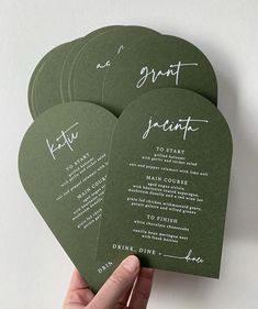 hand holding four green wedding program cards with white writing on them, in front of a white background