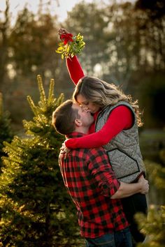 a man and woman are kissing in front of a christmas tree at the same time