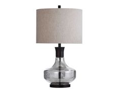 a glass table lamp with a beige shade on it's side and a black base