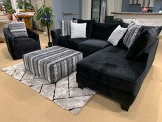 a living room filled with black couches and pillows on top of a white rug