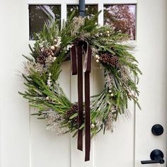 a wreath on the front door with pine cones, berries and evergreens hanging from it