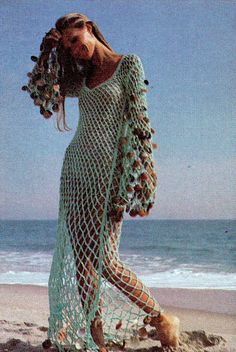 a woman is walking on the beach wearing a crochet dress with shells in it