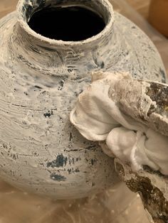 a white vase sitting on top of a table covered in dirt and plastic wrappers