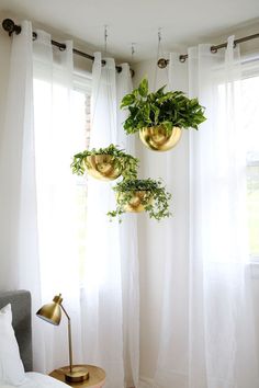 two hanging planters in the corner of a bedroom with white drapes and curtains