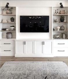 a living room with white cabinets and a large tv on top of the entertainment center