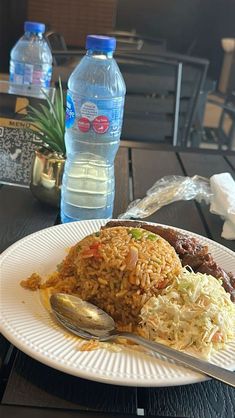 a white plate topped with rice and meat on top of a table next to water bottles