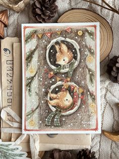 a christmas card with two cats in the snow and pine cones on top of it