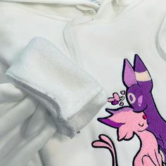 a white hoodie with an image of a purple cat on the front and pink kitten on the back