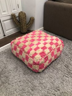 a pink and white square pouffle sitting on the floor next to a cactus