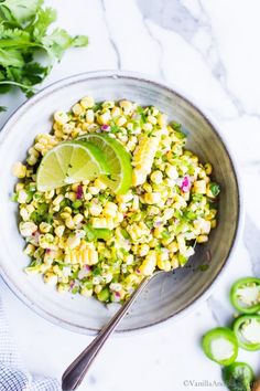 a bowl filled with corn and limes on top of a white marble countertop