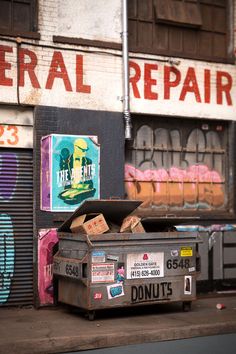 an old box sitting on the side of a road in front of a building that has graffiti all over it