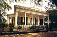 a large white house with columns and pillars on the front porch, surrounded by trees