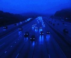 cars driving down the highway at night in heavy rain and smoggy skies with blue hues