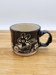 a black and white coffee cup on a wooden table with an animal drawn on it