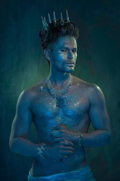 a man with silver paint on his face and chest is standing in front of a dark background