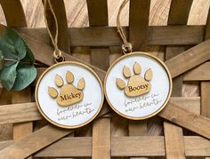 two personalized pet memorial ornaments hanging on a wooden fence with greenery in the background