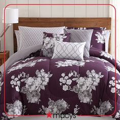 a bed with purple and white flowers on the comforter, pillows and pillow cases