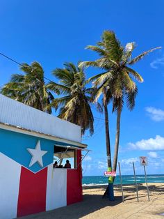 a red, white and blue building on the beach with palm trees