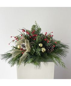 a white vase filled with pine cones and greenery