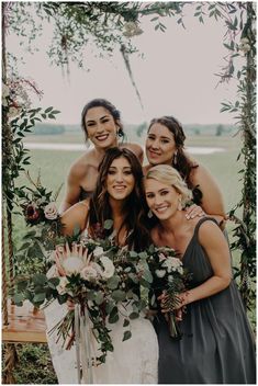 the bride and her bridesmaids pose for a photo in front of an arch decorated with greenery