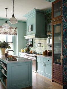 a kitchen with blue cabinets and wooden floors is pictured in this image, there are two hanging lights above the island