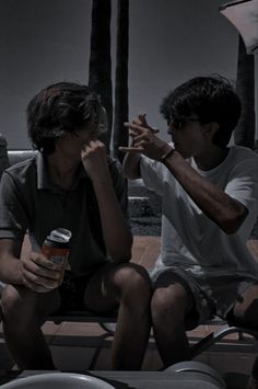 two people sitting on a bench talking and drinking