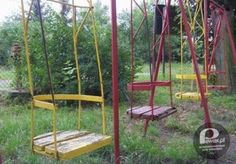 two swings in the grass near some bushes and trees, one is yellow and the other is red