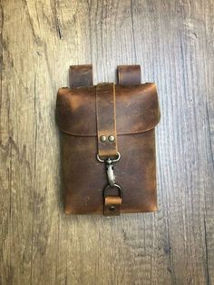 a small brown leather pouch with a metal hook on the front and two straps attached to it