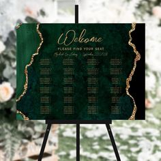 a green and gold wedding seating chart on a easel with flowers in the background