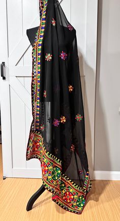 This black Navaratri dupatta features delicate thread work and glimmering mirrors, adding an elegant touch to any outfit. Made from georgette fabric, it is lightweight and comfortable to wear during festive occasions. Enhance your style and make a statement with this beautiful dupatta. Black Chanderi Saree For Navratri, Black Traditional Wear With Mirror Work For Navratri, Traditional Black Saree With Sheer Dupatta, Black Semi-stitched Bohemian Saree, Black Dupatta With Motifs For Navratri, Black Saree With Mirror Work For Navratri, Black Chanderi Saree With Mirror Work, Black Chanderi Traditional Wear With Mirror Work, Navratri Black Dupatta With Motifs